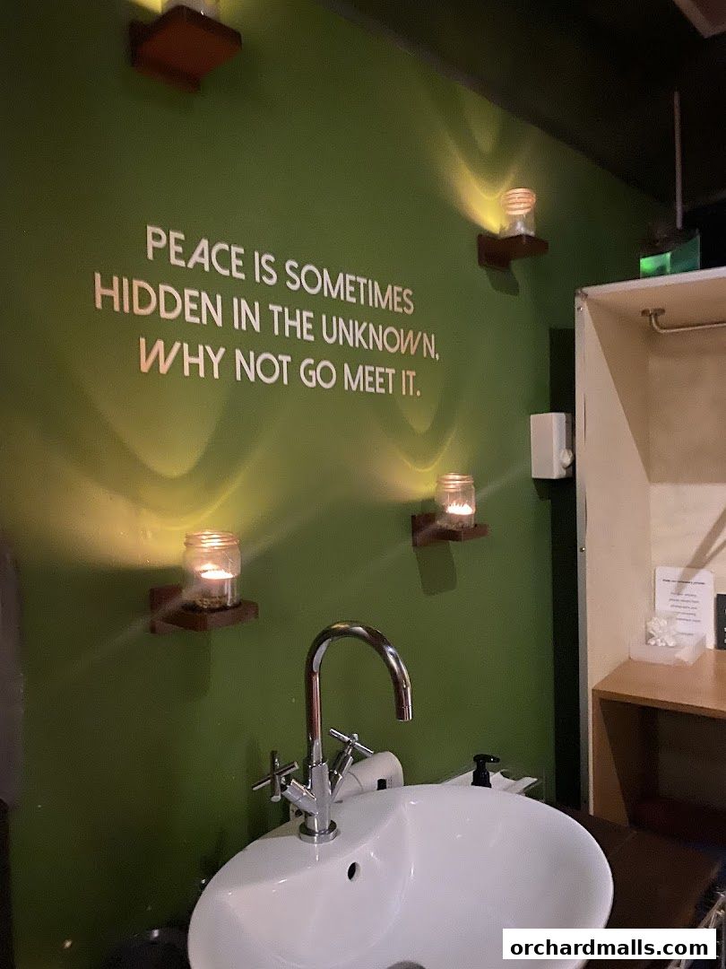 A sink with a modern faucet against a green wall with a quote and candles.
