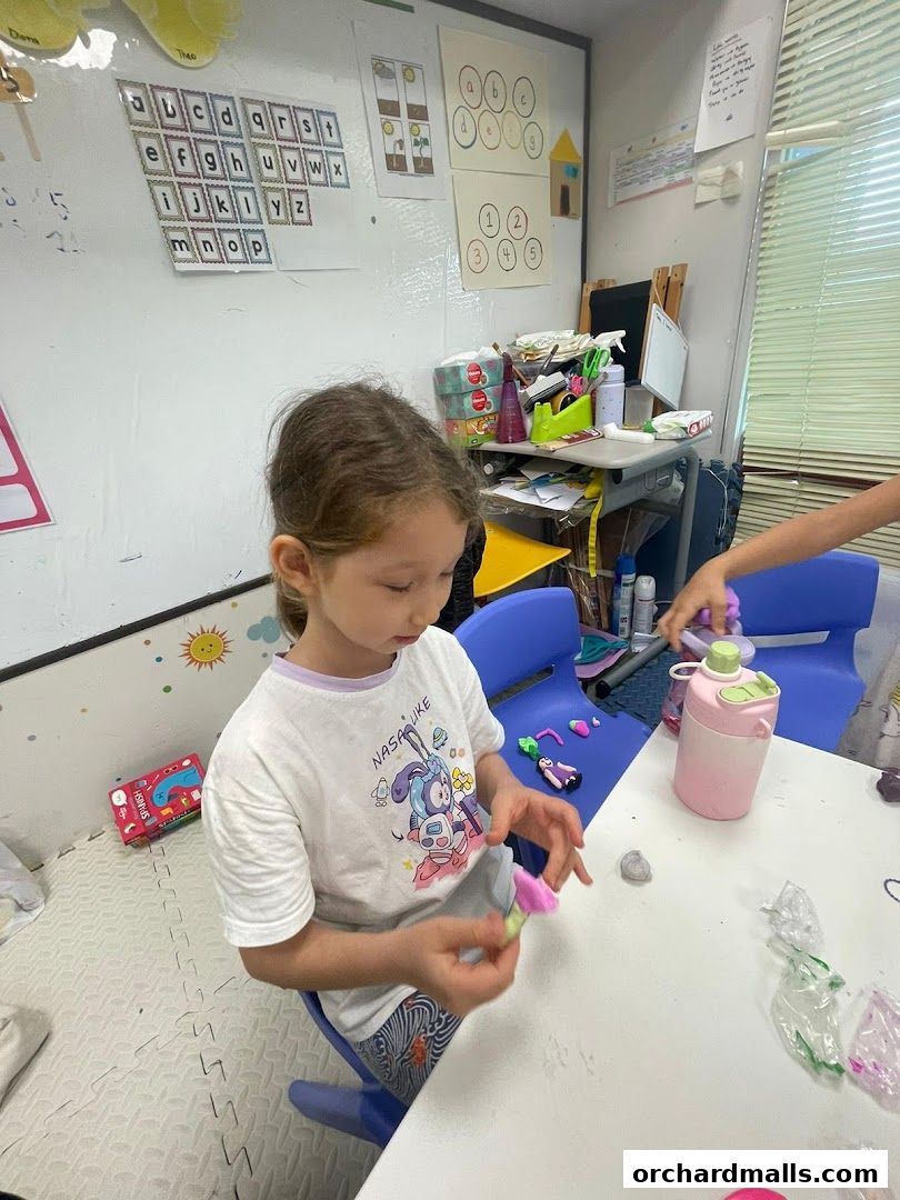 A young girl is engaged in a craft activity at a table in a classroom.