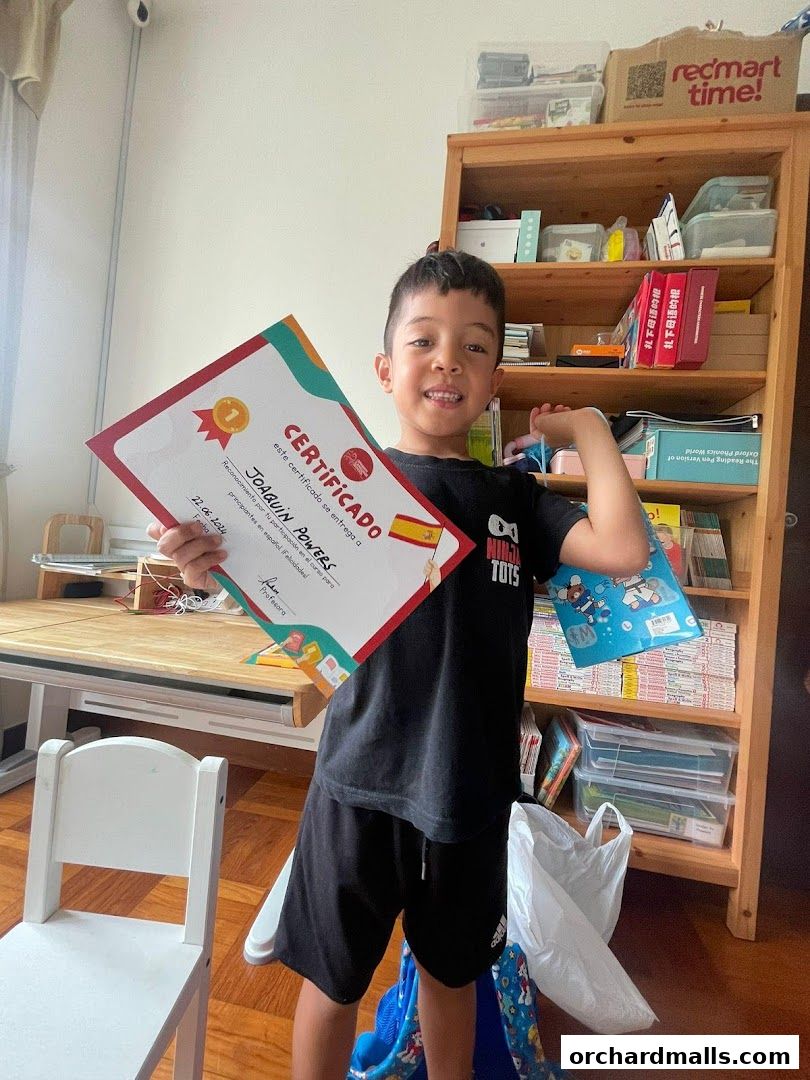 A young boy proudly holds a Spanish language certificate, smiling at the camera.