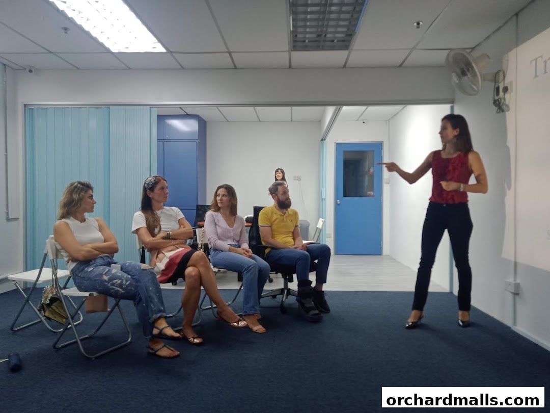 A teacher points to a screen while students listen in a classroom setting.