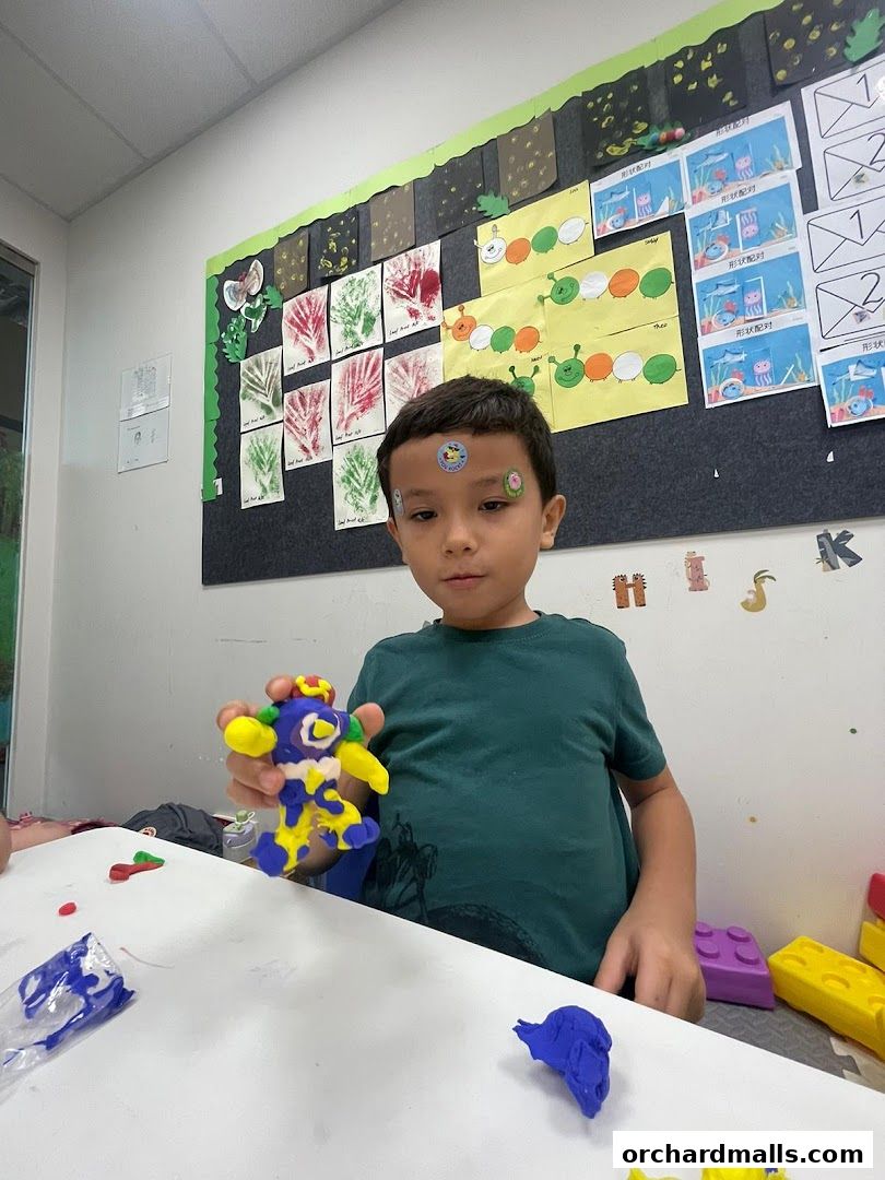 A young boy proudly displays a colorful clay creation in a classroom setting.