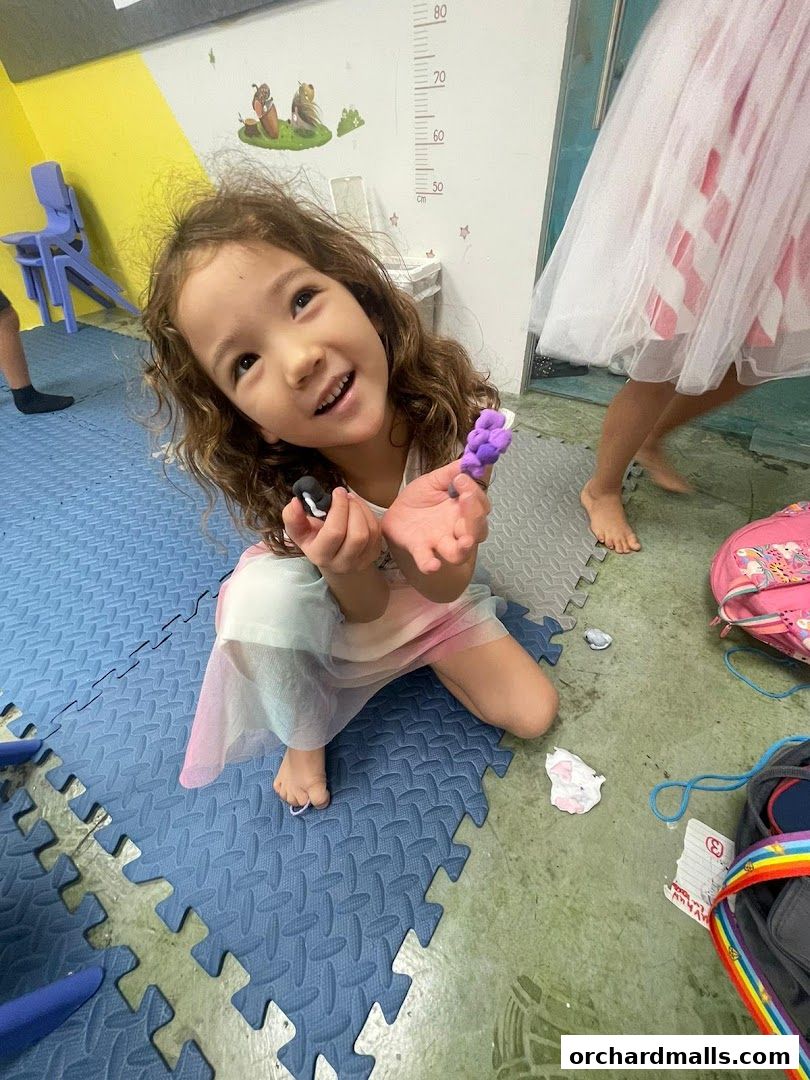 A young girl smiles while holding colorful clay figures in a classroom setting.