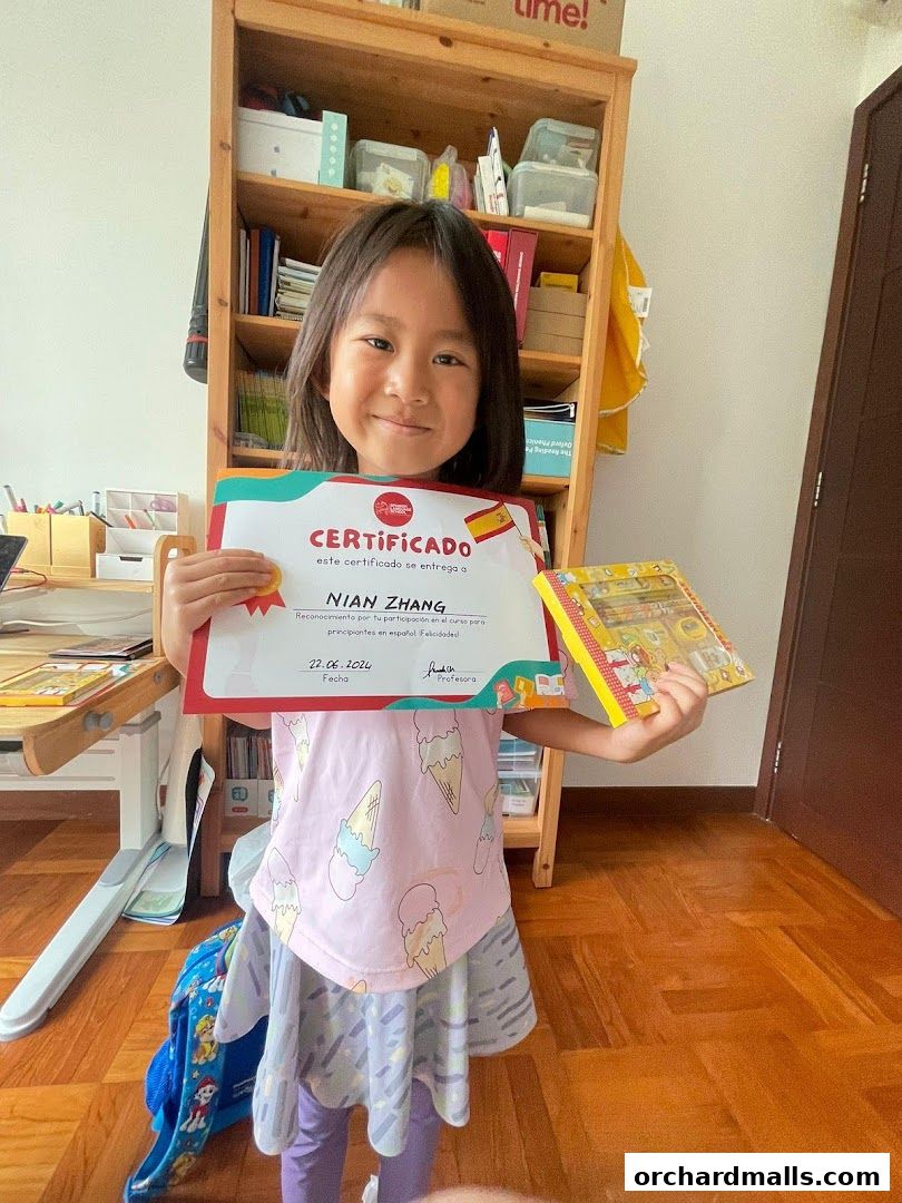 A young girl proudly holds a Spanish language certificate and a small gift.