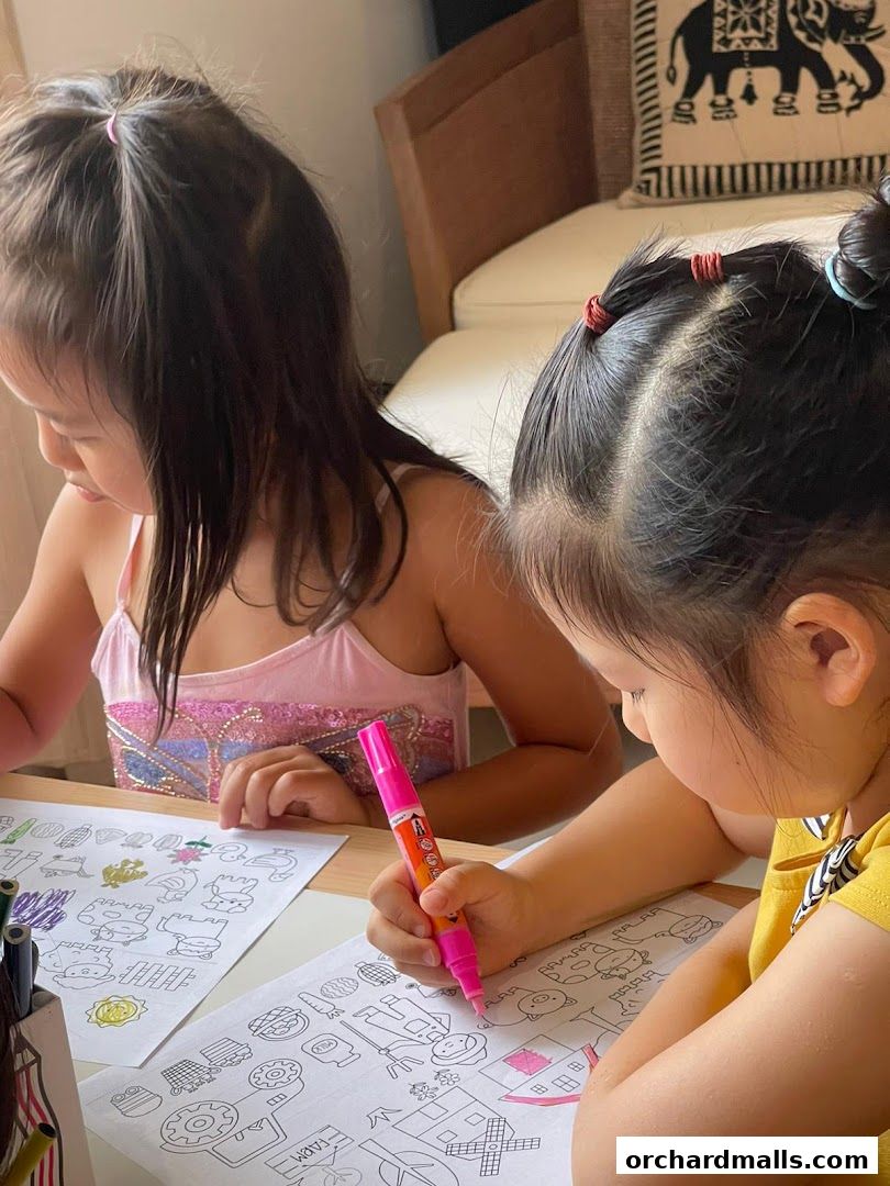 Two young girls are coloring pictures with markers at a table.