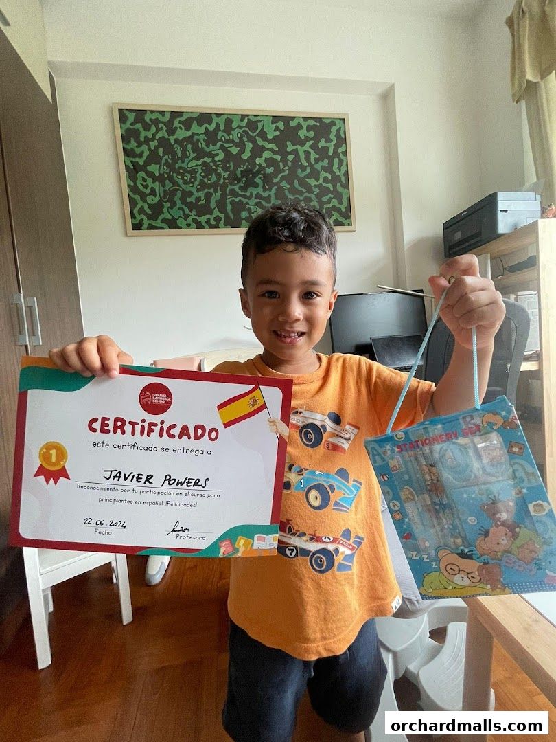 A smiling boy holds a Spanish language certificate and a stationery set.
