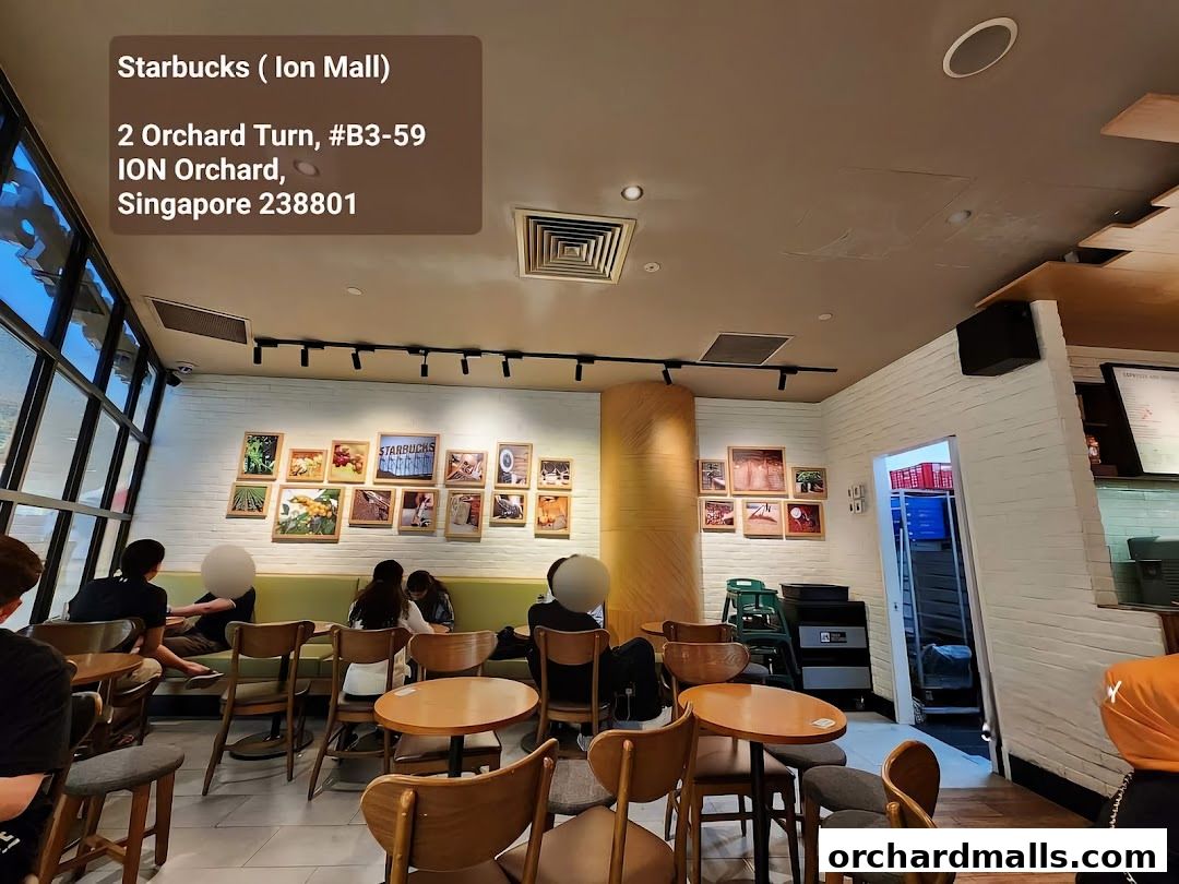 Interior view of a Starbucks cafe with customers seated at tables and artwork on the wall.