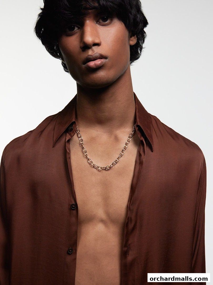 A man wearing a brown silk shirt and a gold chain necklace.