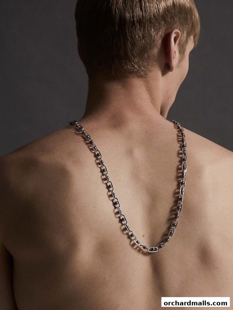 A man's back wearing a silver chain necklace with oval links and small beads.