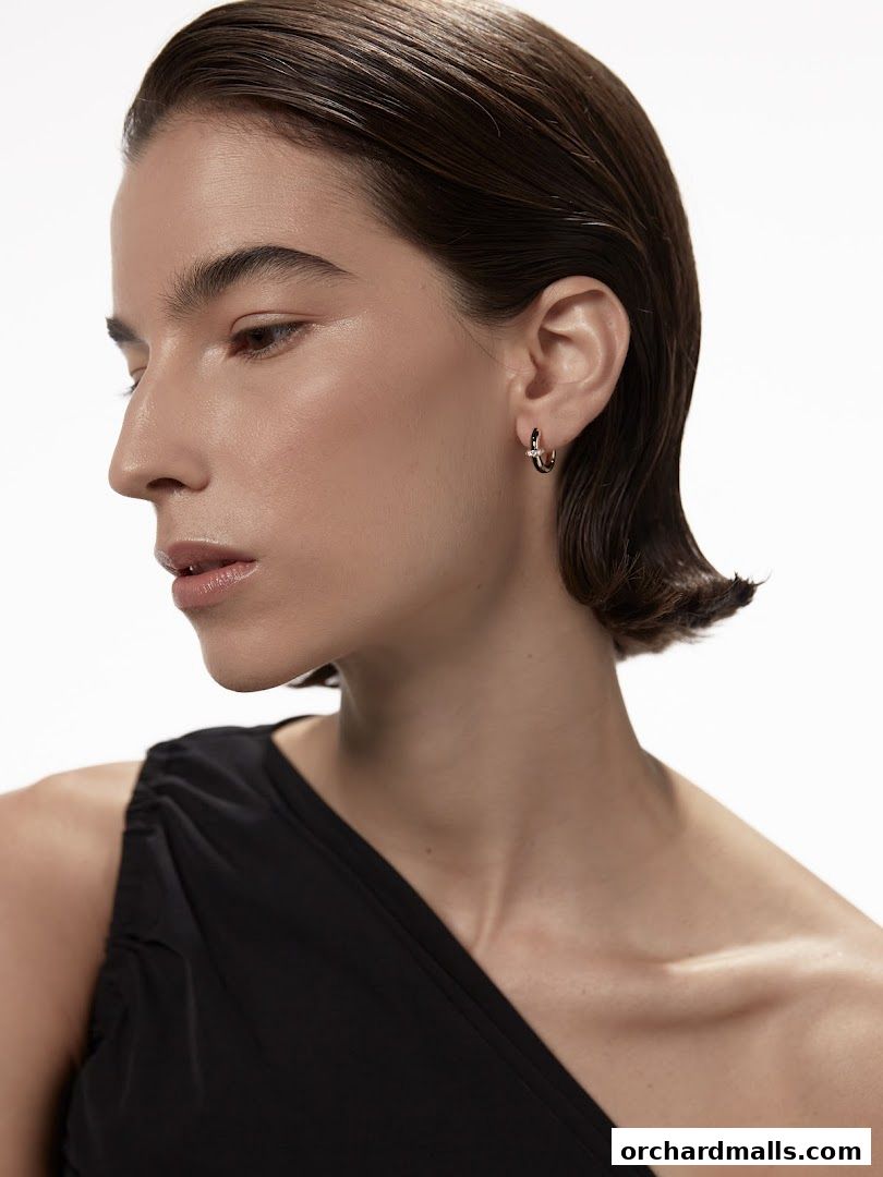 A woman models a gold hoop earring with a small diamond accent.