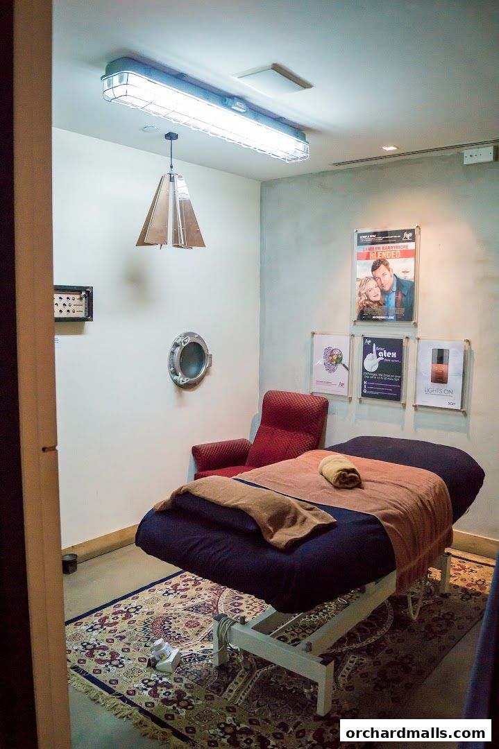 A treatment room with a massage bed, chair, and decorative posters on the wall.