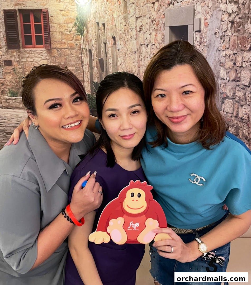 Three smiling women pose for a photo, one holding a red monkey cutout.