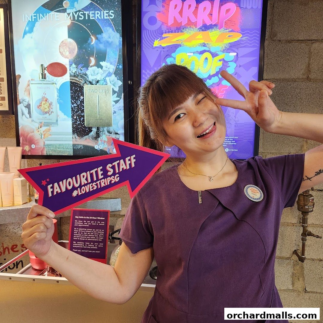 A smiling staff member holds a 'Favourite Staff' sign in front of promotional posters.