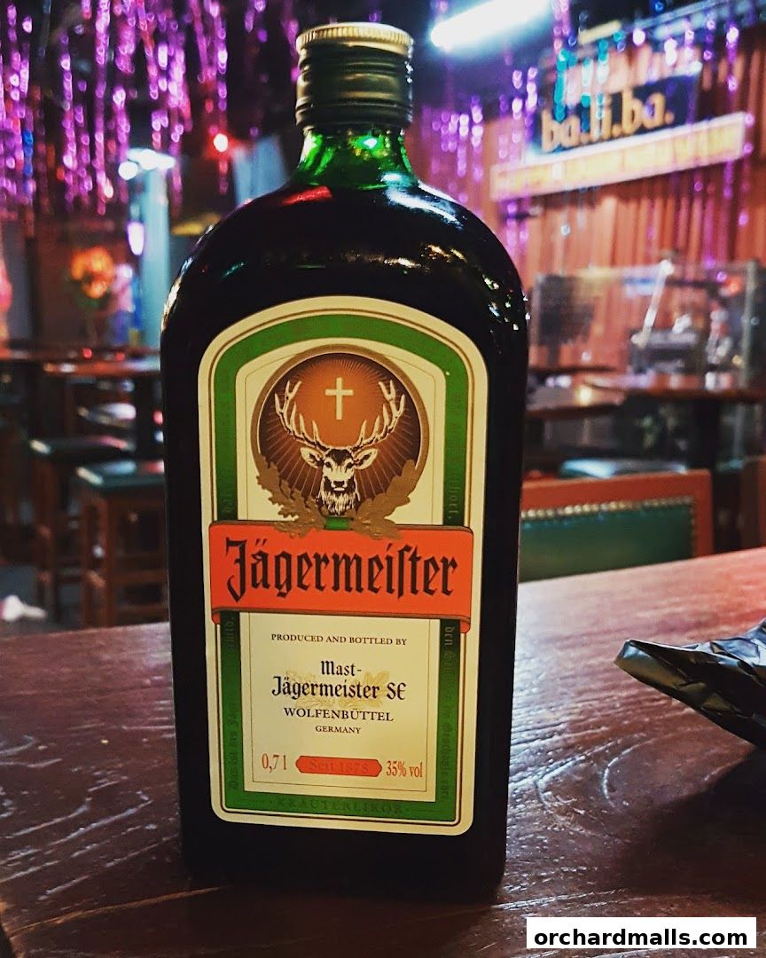 A bottle of Jägermeister sits on a wooden bar with a blurred background.