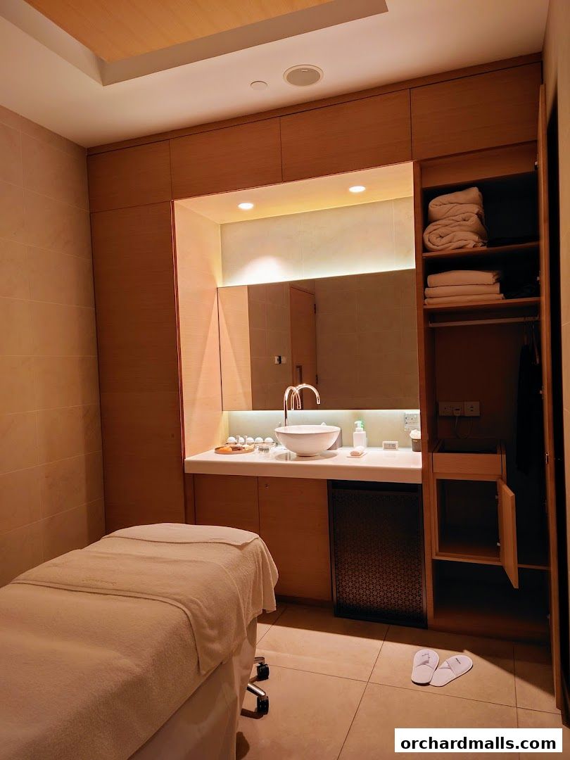 A clean and modern spa room with a massage bed, sink, and storage cabinets.