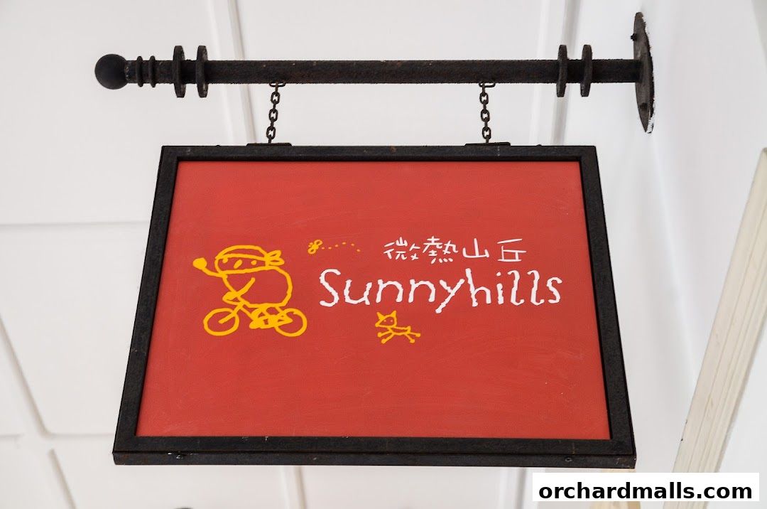 A red sign with the name Sunnyhills and cartoon drawings hangs from a metal bracket.