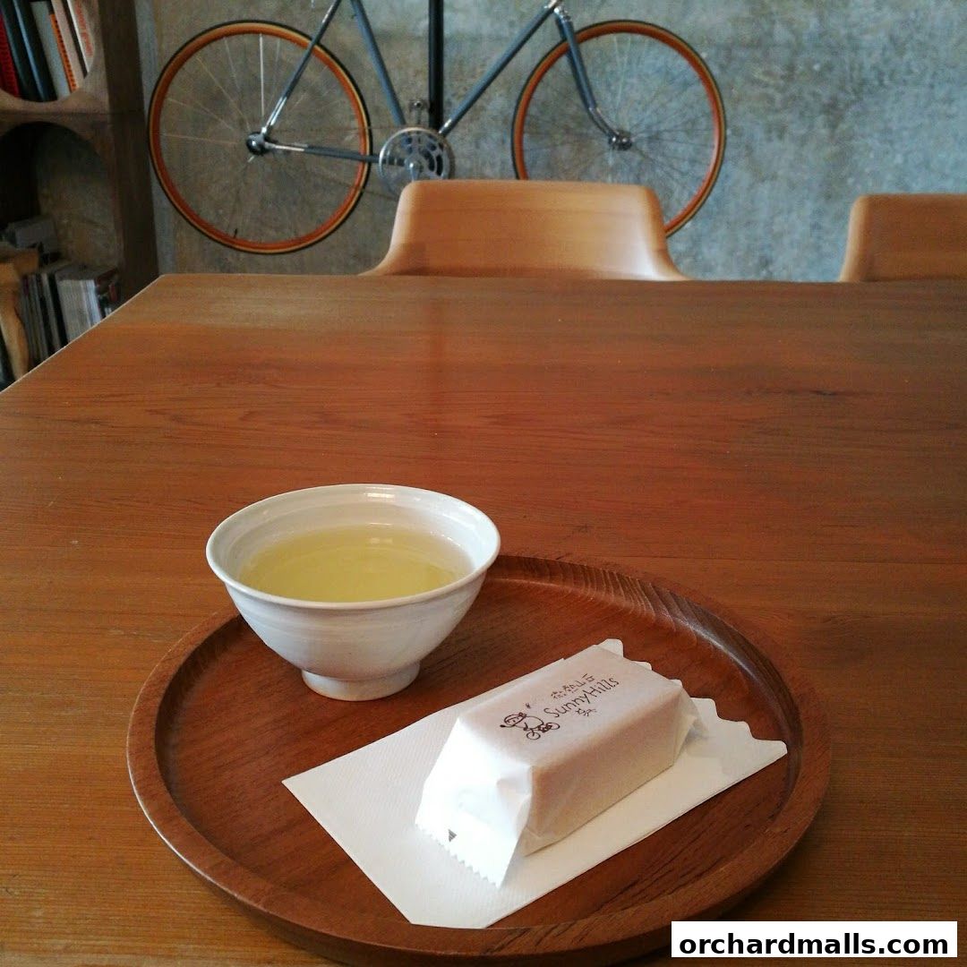 A cup of tea and a wrapped pastry on a wooden tray, with a bicycle mounted on the wall.
