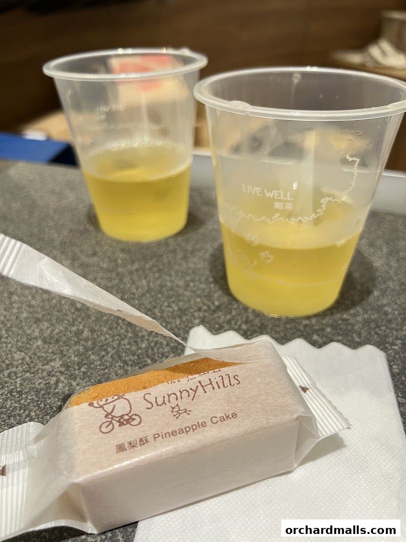 A SunnyHills Pineapple Cake is presented with two cups of beverage.
