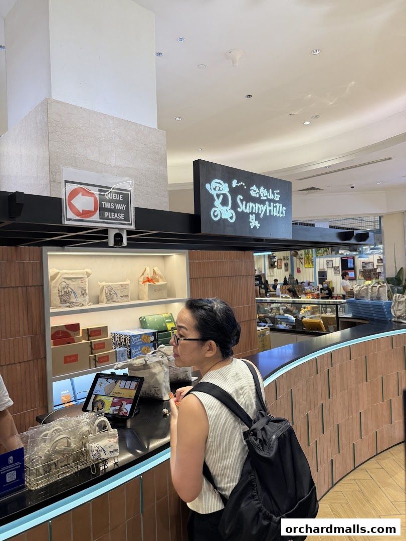 A woman queues at the SunnyHills Orchard counter, with products displayed on shelves.