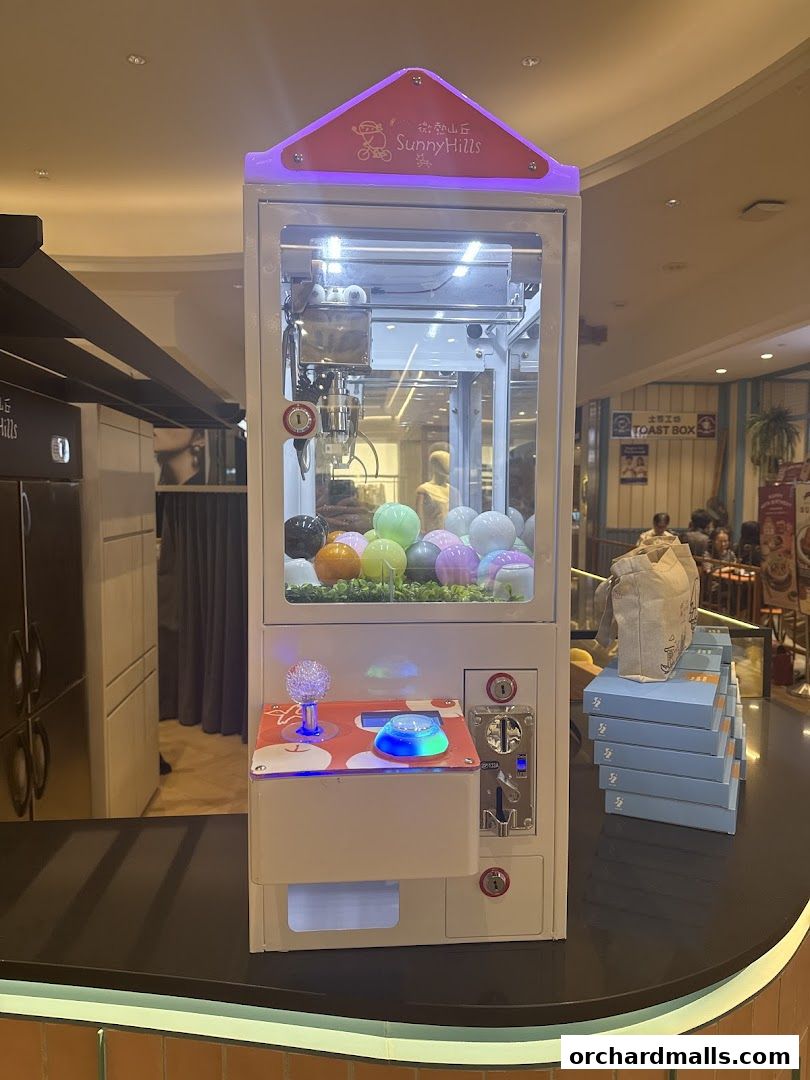 A claw machine with colorful prizes inside, branded with SunnyHills Orchard.