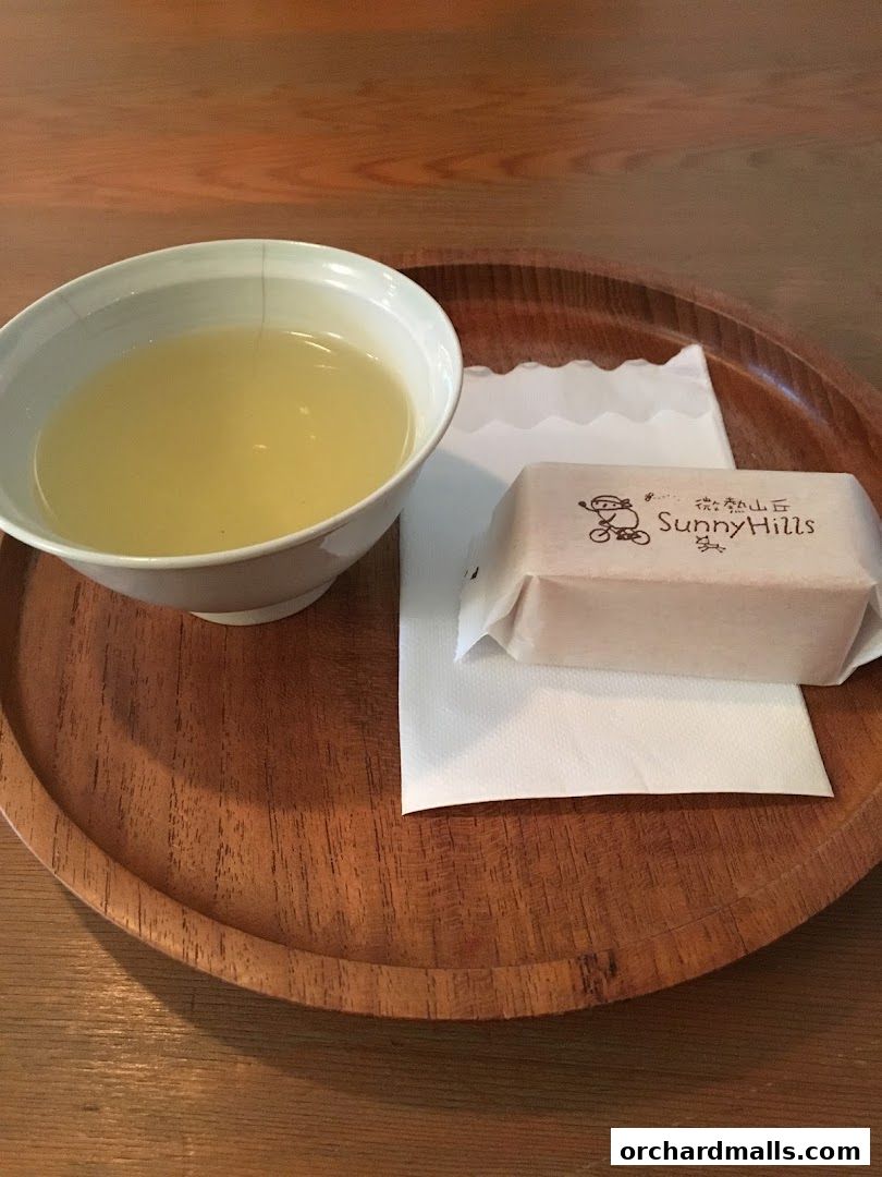 A cup of tea and a wrapped pastry on a wooden tray.