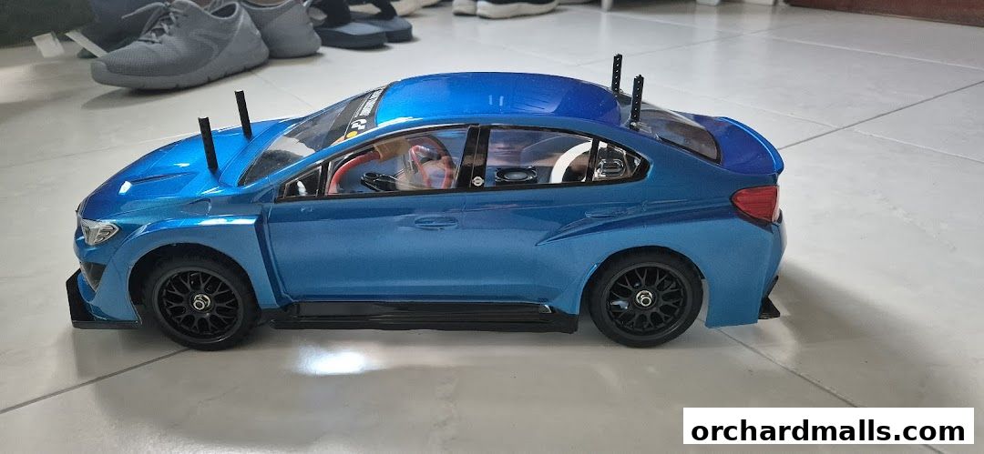 A detailed blue remote-controlled car with racing modifications sits on a tiled floor.