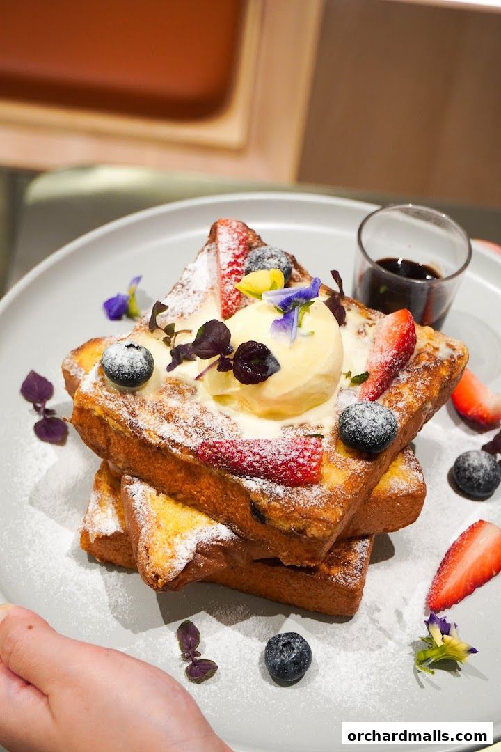 A stack of French toast topped with ice cream, berries, and edible flowers.