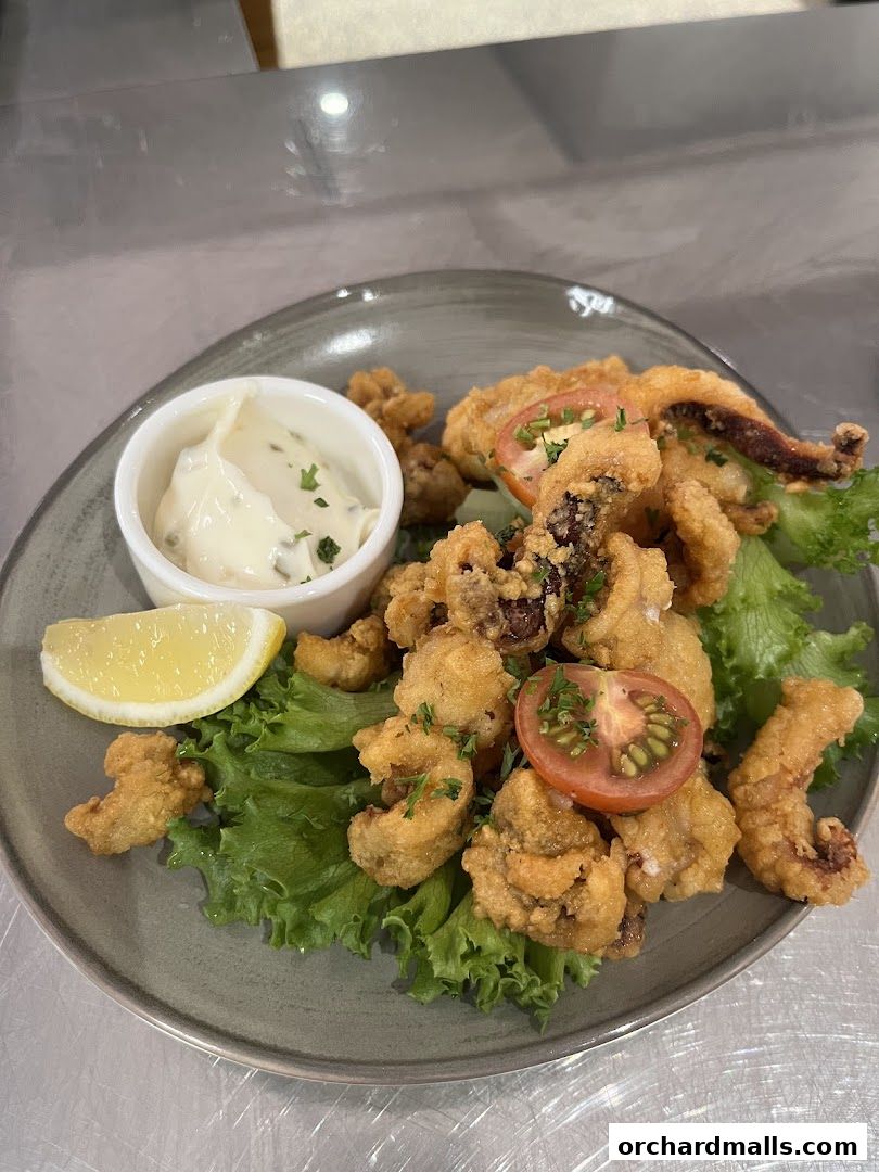 A plate of crispy fried calamari served with a lemon wedge and dipping sauce.