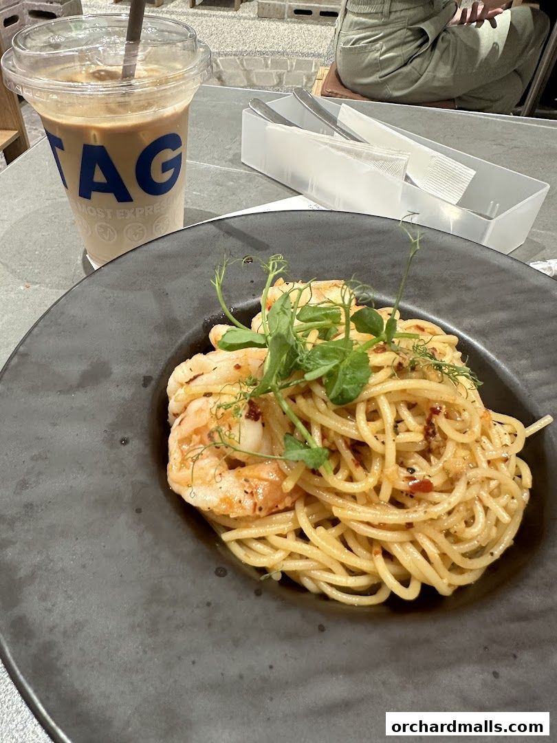 A plate of shrimp pasta and an iced coffee with the TAG logo.