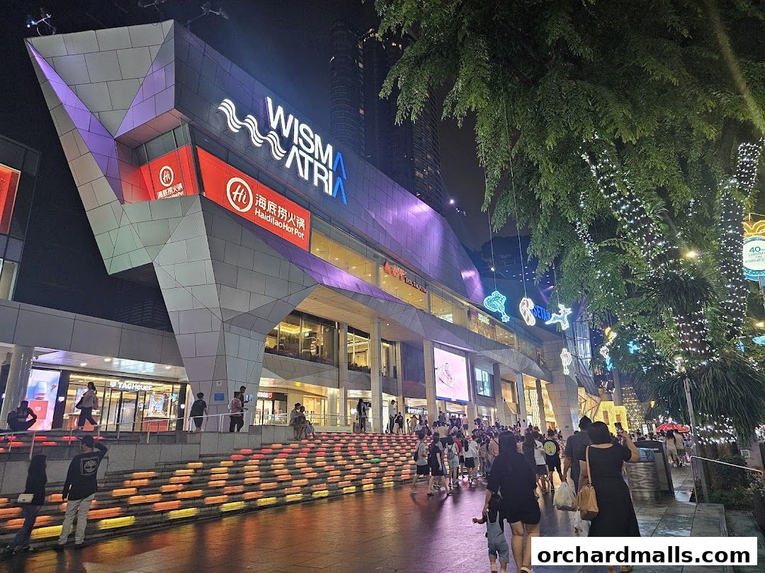 A nighttime view of the Wisma Atria shopping mall entrance with a TAG Heuer store visible.