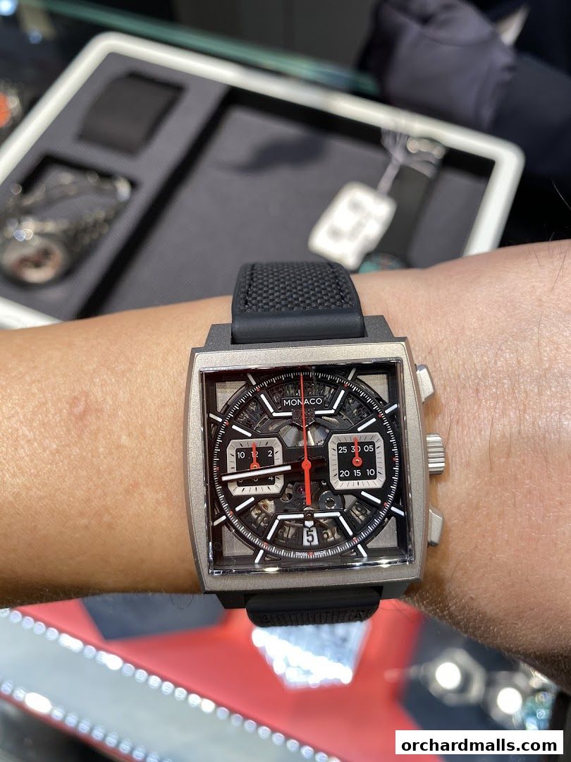 A person wearing a TAG Heuer Monaco watch with a skeleton dial and black strap.