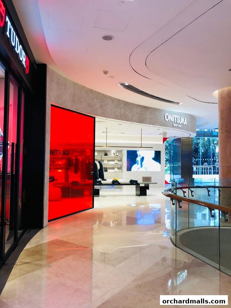Interior view of a modern shopping mall with a Tudor store and an Onitsuka Tiger store.