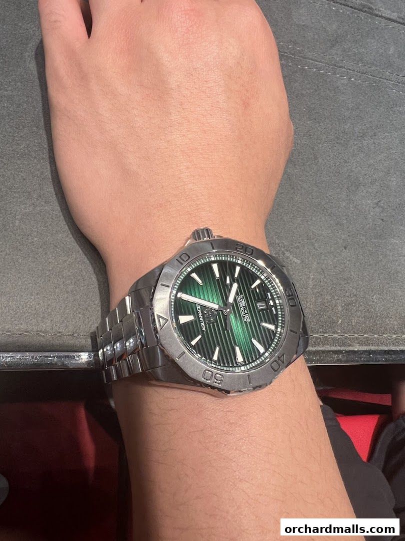 A person's wrist wearing a TAG Heuer Aquaracer watch with a green dial.