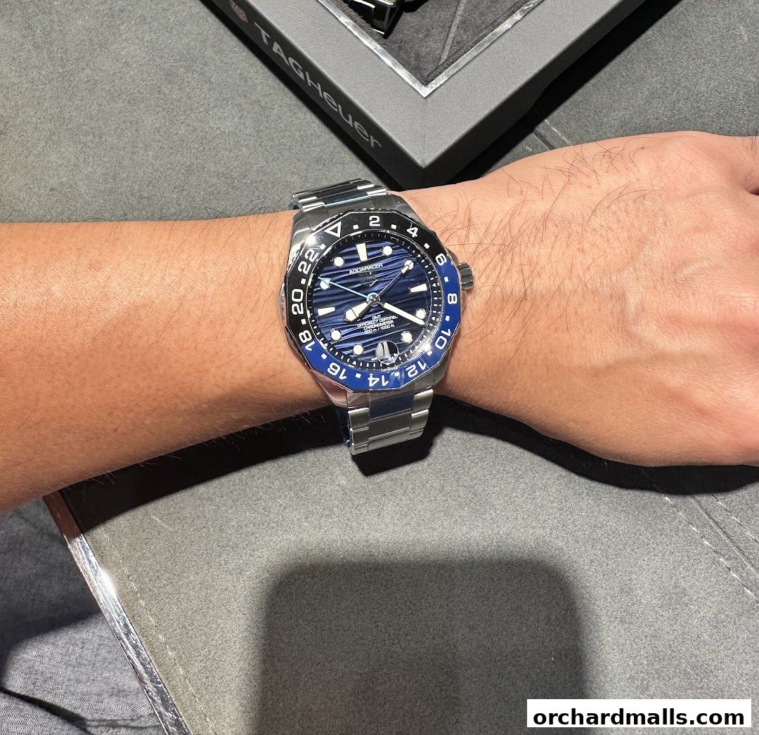 A person wears a TAG Heuer Aquaracer watch with a blue dial and a bi-color bezel.