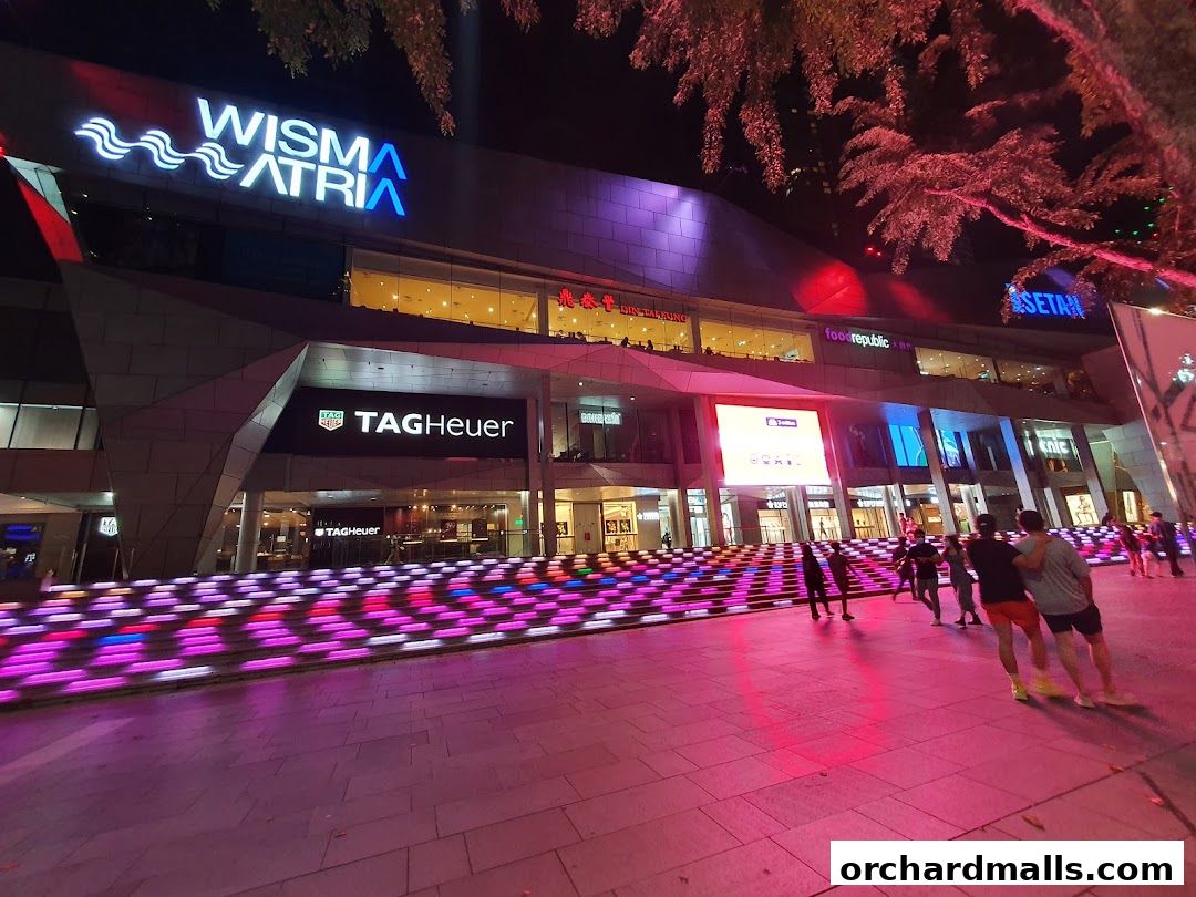 The TAG Heuer store is visible at night in a brightly lit shopping mall with colorful stairs.