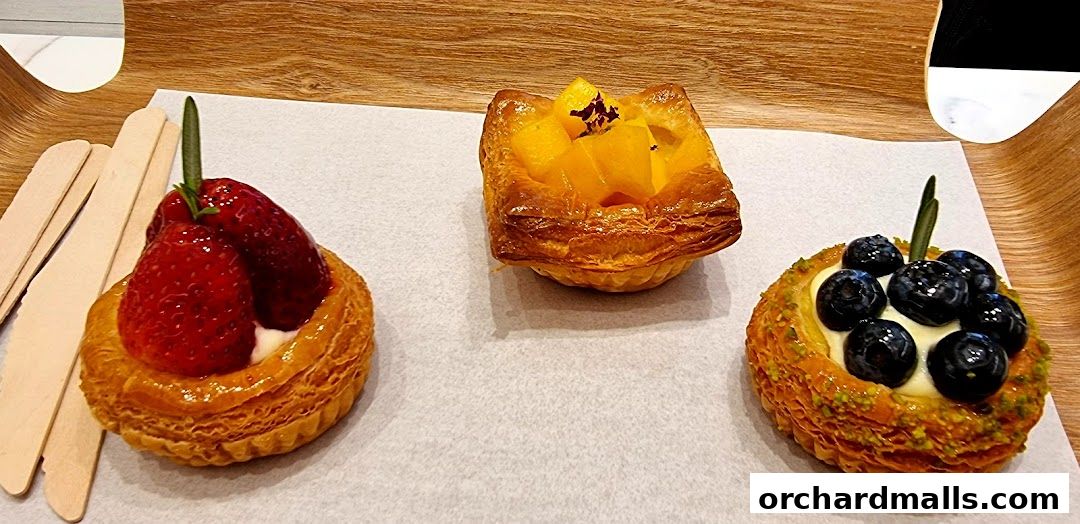 Three delicious pastries: strawberry, mango, and blueberry, presented on a wooden tray.