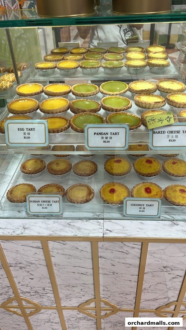 A display case filled with various freshly baked tarts, including egg, pandan, and durian cheese.