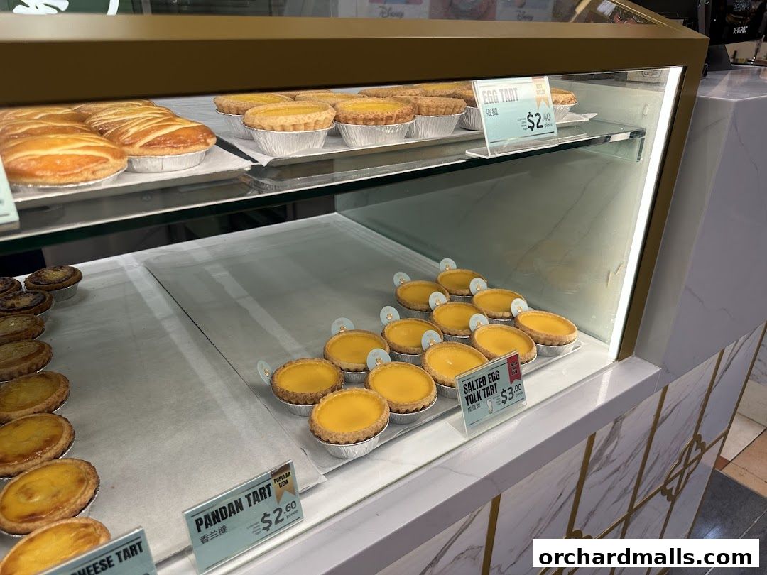 A display case filled with various freshly baked tarts, including egg tarts and pandan tarts.