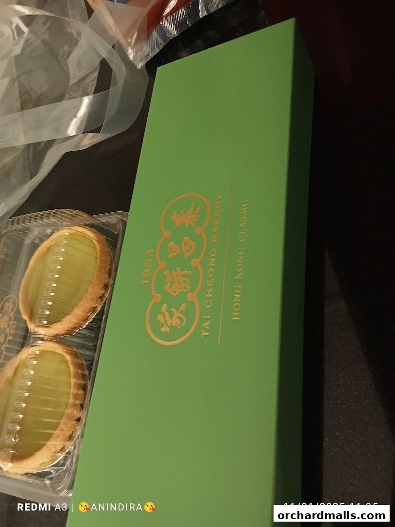 A green box from Tai Cheong Bakery with two egg tarts in a plastic container.