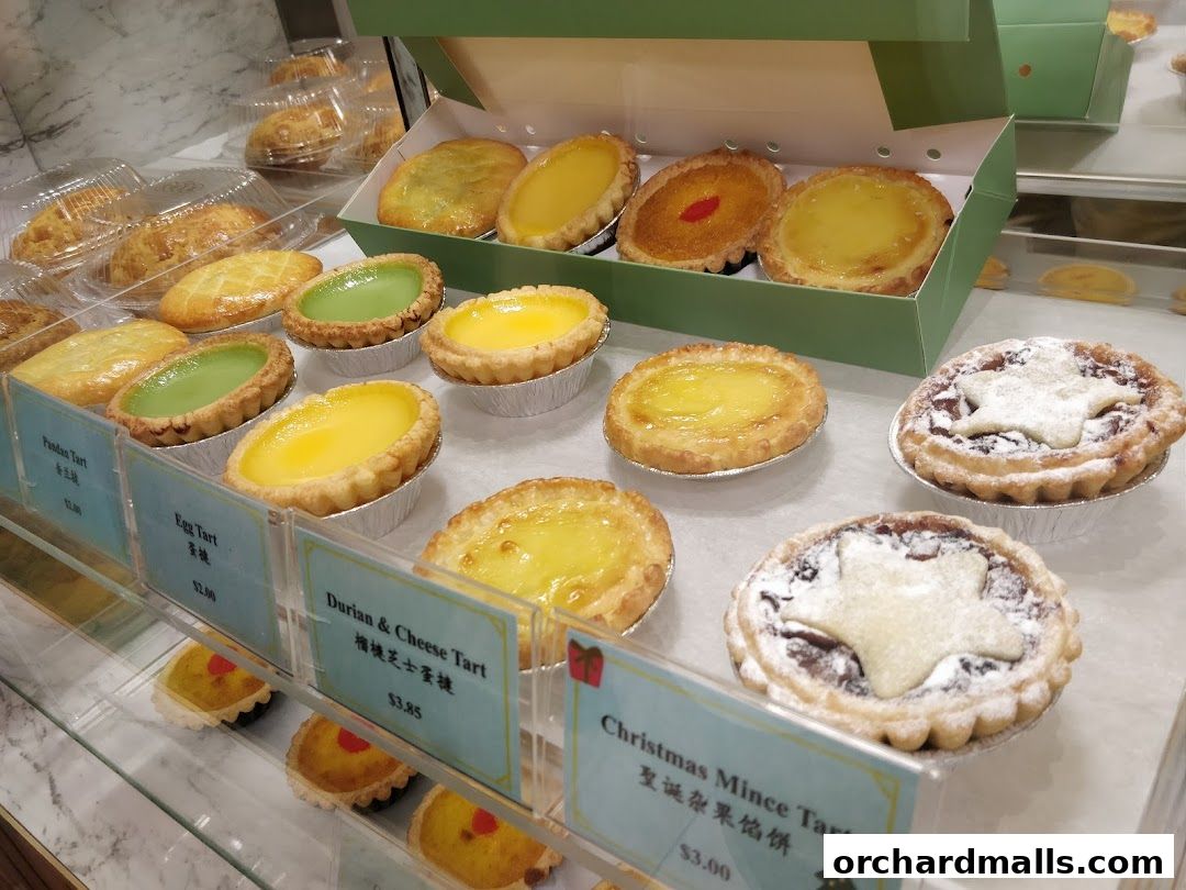A display of various tarts, including egg, pandan, durian & cheese, and Christmas mince tarts.