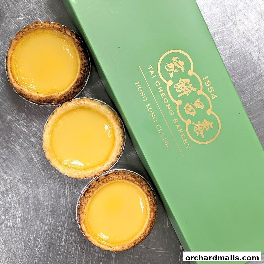 Three delicious egg tarts next to a green Tai Cheong Bakery box.