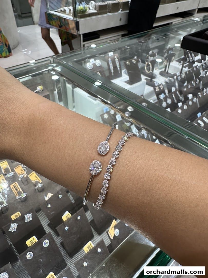 A person's arm adorned with two sparkling diamond bracelets in a jewelry store display.