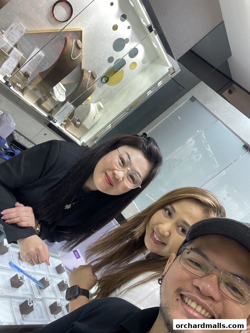 Three smiling people in a jewelry store, with display cases of necklaces and rings.