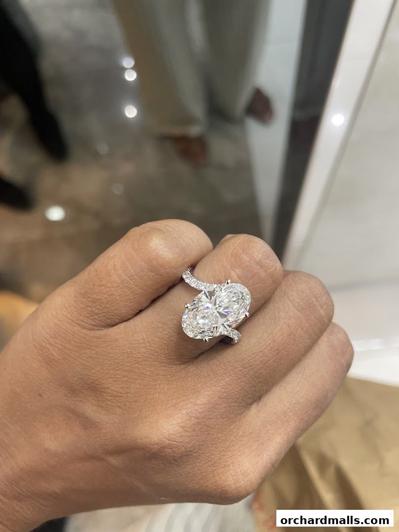 A hand wearing a stunning oval-cut diamond ring with a diamond-encrusted band.