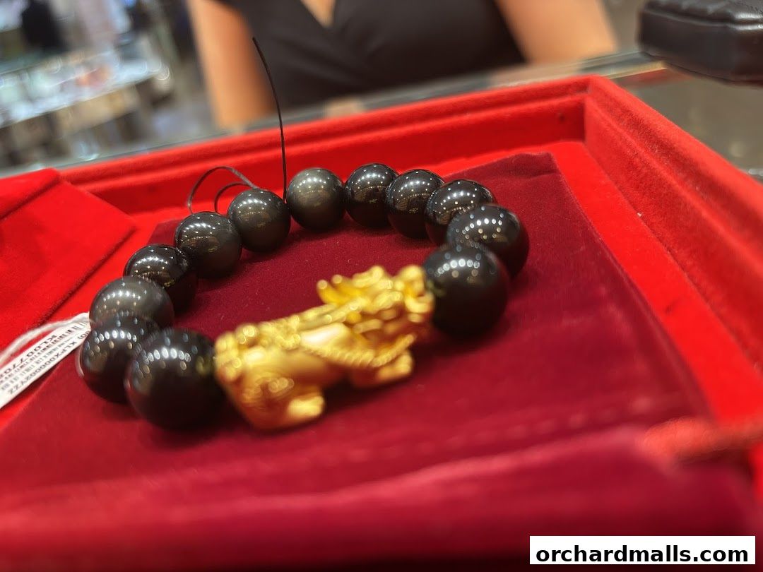 A close-up of a black beaded bracelet with a gold Pixiu charm on a red velvet display.