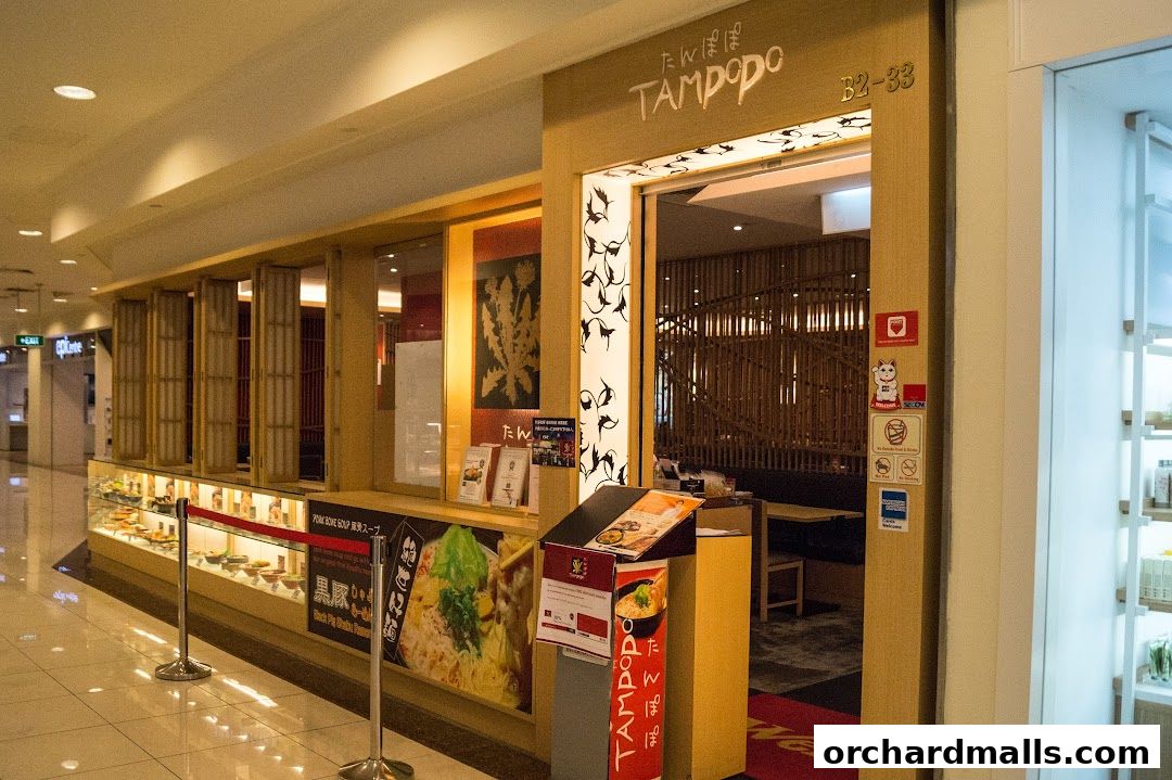 The entrance of Tampopo, a Japanese restaurant, with a display of food and a menu stand.