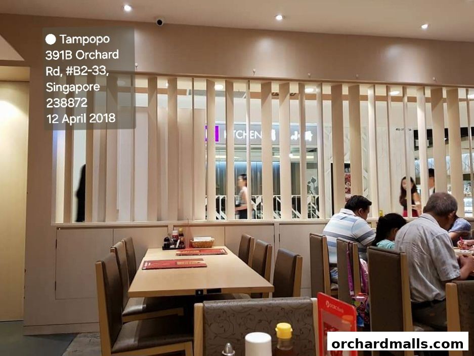 Interior view of Tampopo restaurant with diners seated at tables and a view of the kitchen.