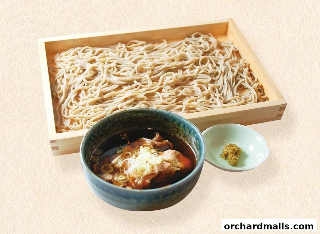 A wooden tray of soba noodles served with a dipping sauce and a small dish of wasabi.