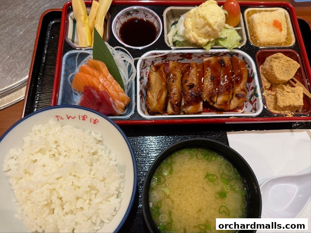 A bento box meal featuring teriyaki chicken, sashimi, rice, miso soup, and dessert.
