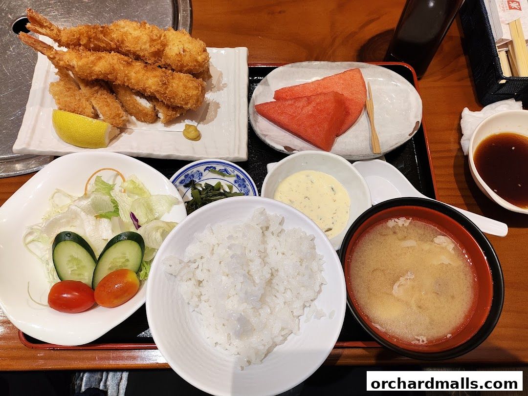 A delicious Japanese meal featuring fried shrimp, rice, salad, miso soup, and watermelon.