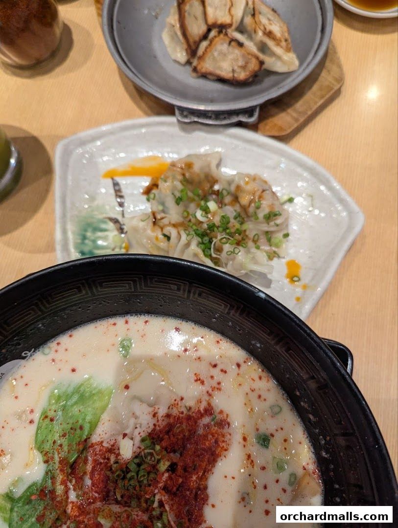 A close-up of a creamy ramen bowl with dumplings and a side of pan-fried gyoza.